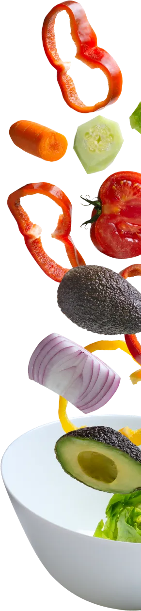 Świeże, krojone warzywa: papryka, marchew, ogórek, awokado, cebula, wpadają do miski.